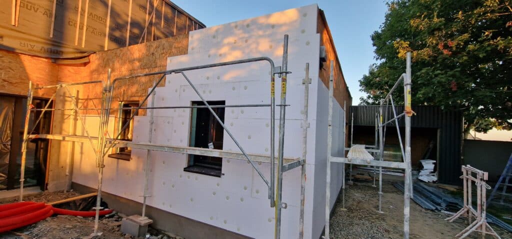 Maison en construction avec pose d'isolation extérieure en polystyrène et échafaudages. L'écran sous-toiture COUVE-AIR est visible, sous le soleil couchant.